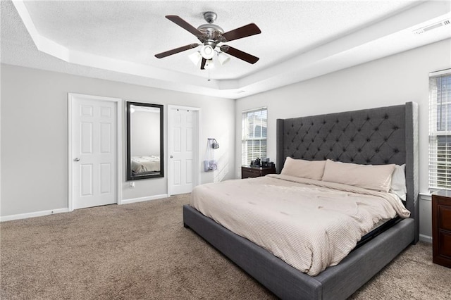 bedroom with a raised ceiling, light colored carpet, and ceiling fan