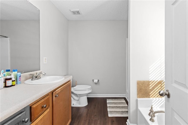 bathroom featuring hardwood / wood-style flooring, vanity, a textured ceiling, a tub to relax in, and toilet