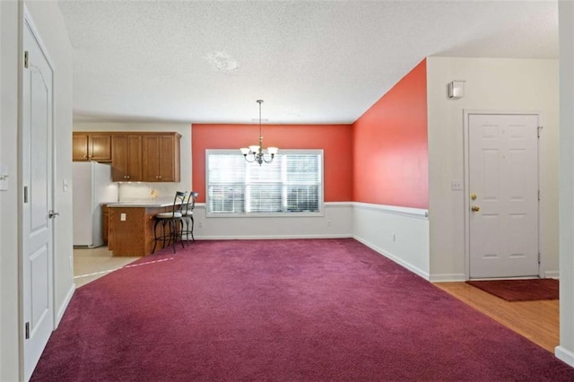 kitchen featuring a textured ceiling, decorative light fixtures, light colored carpet, a chandelier, and white fridge