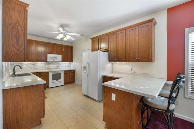 kitchen with sink, a breakfast bar area, ceiling fan, kitchen peninsula, and white appliances