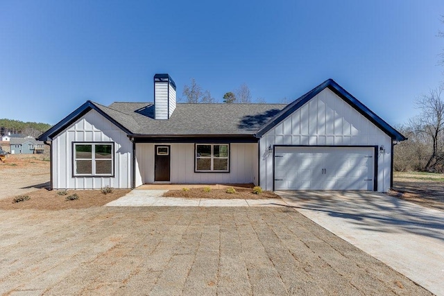 modern farmhouse with a garage, driveway, a chimney, roof with shingles, and board and batten siding