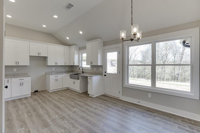 kitchen with lofted ceiling, light wood-style flooring, white cabinetry, and a sink