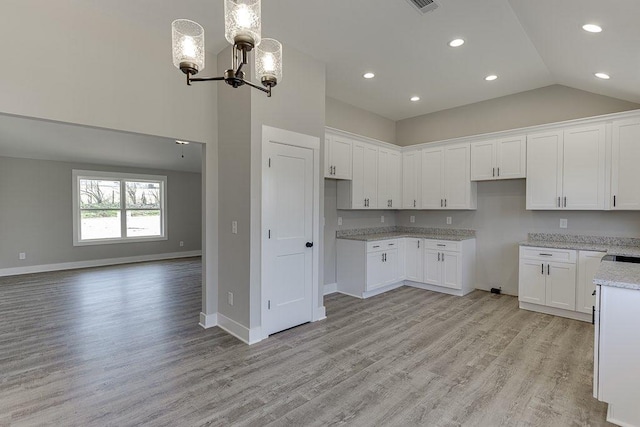 kitchen featuring light stone counters, light wood-style flooring, white cabinetry, a chandelier, and baseboards