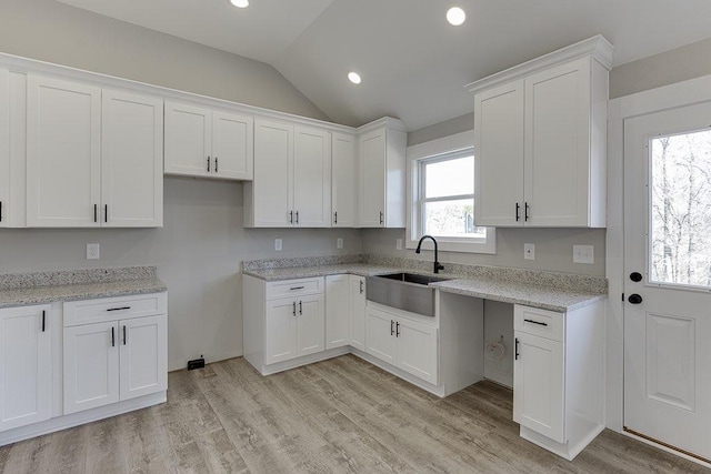 kitchen featuring light wood-style floors, white cabinetry, vaulted ceiling, and a sink