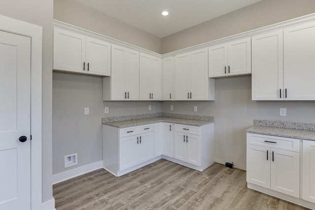 kitchen featuring light stone counters, light wood finished floors, and white cabinetry