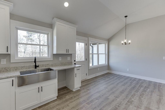 kitchen with light wood finished floors, white cabinetry, vaulted ceiling, and a sink