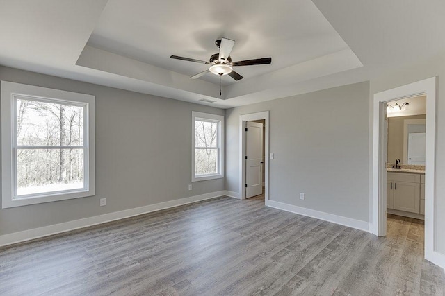 unfurnished bedroom with light wood-style flooring, visible vents, baseboards, and a raised ceiling