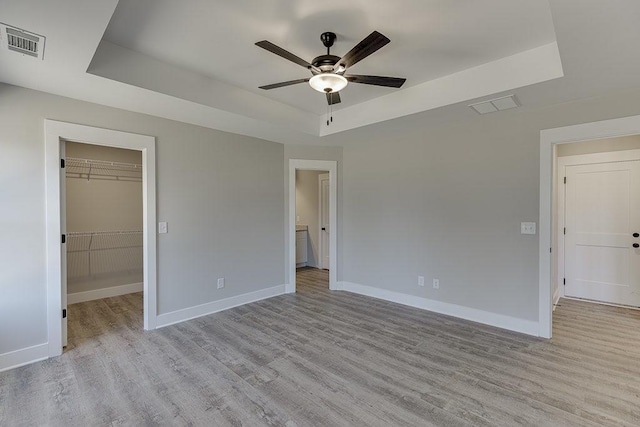 unfurnished bedroom featuring wood finished floors, a raised ceiling, visible vents, and baseboards