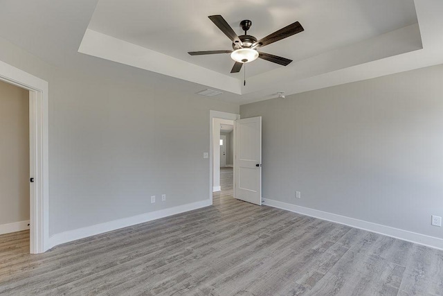 empty room with a tray ceiling, light wood-style flooring, and baseboards