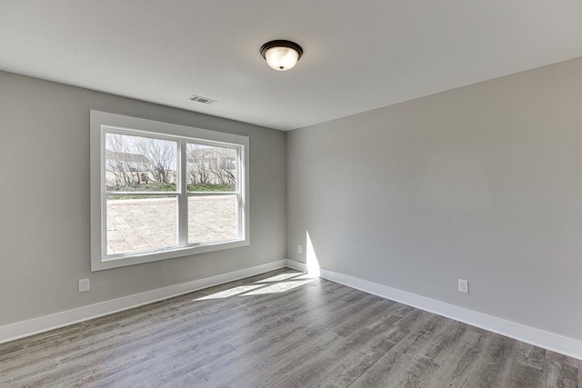 spare room with baseboards, visible vents, and wood finished floors