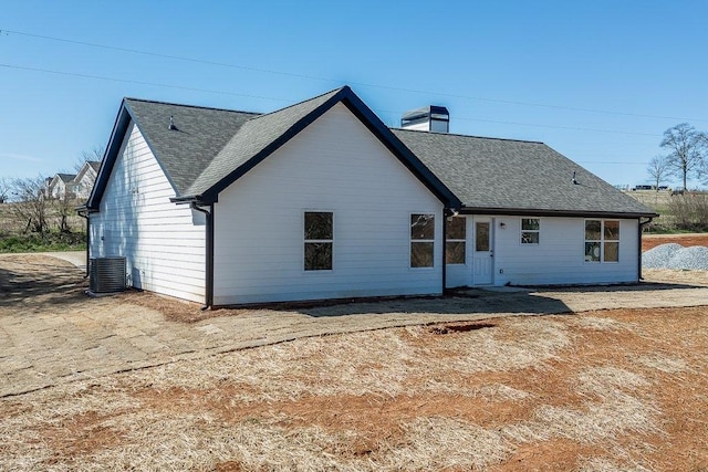 rear view of house with a shingled roof, a chimney, and central AC unit