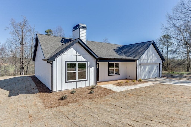 view of front facade with a chimney, a shingled roof, board and batten siding, a garage, and driveway