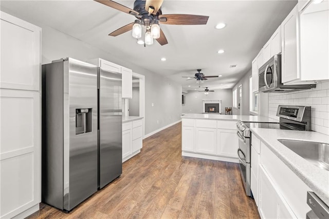 kitchen featuring white cabinets, decorative backsplash, appliances with stainless steel finishes, light hardwood / wood-style floors, and kitchen peninsula