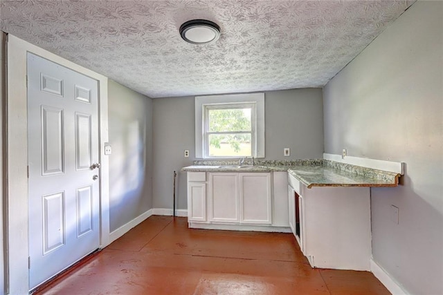 kitchen with baseboards, white cabinetry, light wood-type flooring, a sink, and a textured ceiling