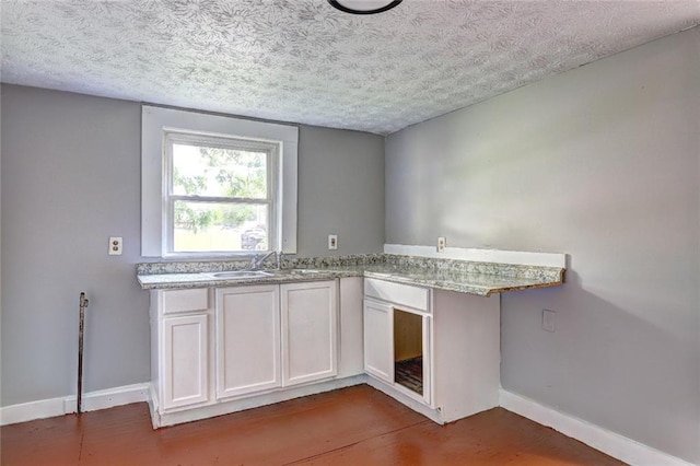 kitchen featuring a textured ceiling, baseboards, a sink, light stone countertops, and dark wood-style flooring