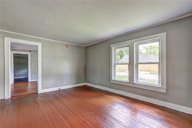 spare room with wood-type flooring, crown molding, and baseboards