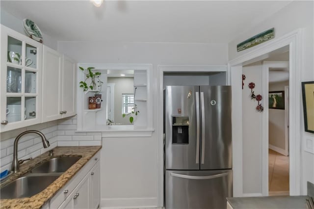 kitchen featuring stone counters, sink, stainless steel fridge with ice dispenser, backsplash, and white cabinets