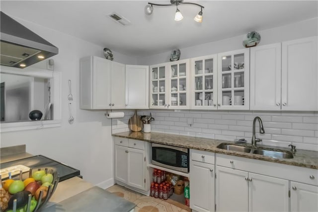 kitchen with range hood, white cabinetry, stainless steel microwave, and sink