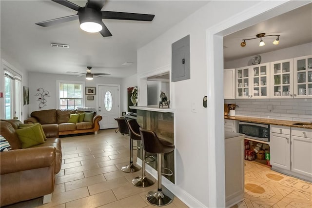 interior space featuring white cabinetry, stainless steel microwave, tasteful backsplash, electric panel, and a breakfast bar