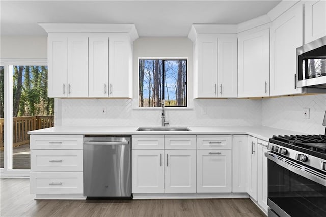 kitchen with stainless steel appliances, hardwood / wood-style flooring, sink, and white cabinets