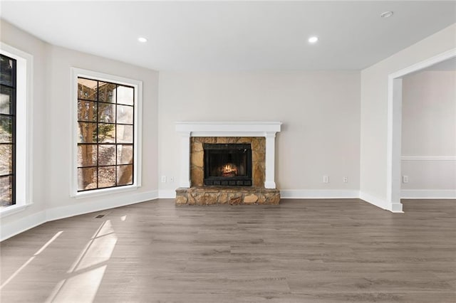 unfurnished living room featuring plenty of natural light, a stone fireplace, and dark hardwood / wood-style flooring