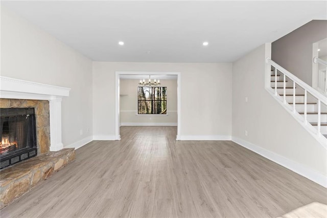 unfurnished living room with an inviting chandelier, a fireplace, and light hardwood / wood-style flooring