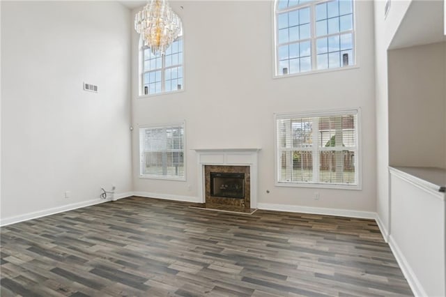 unfurnished living room with a high ceiling, dark wood-type flooring, an inviting chandelier, and a fireplace