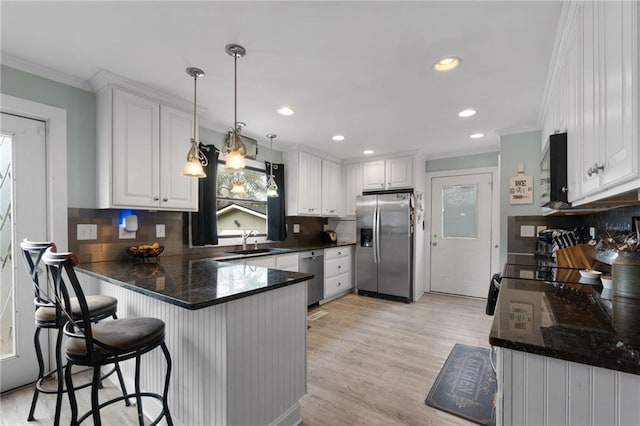 kitchen with appliances with stainless steel finishes, ornamental molding, a peninsula, white cabinetry, and a sink