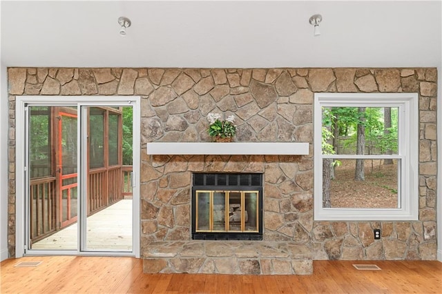 unfurnished living room featuring wood finished floors, healthy amount of natural light, and a stone fireplace