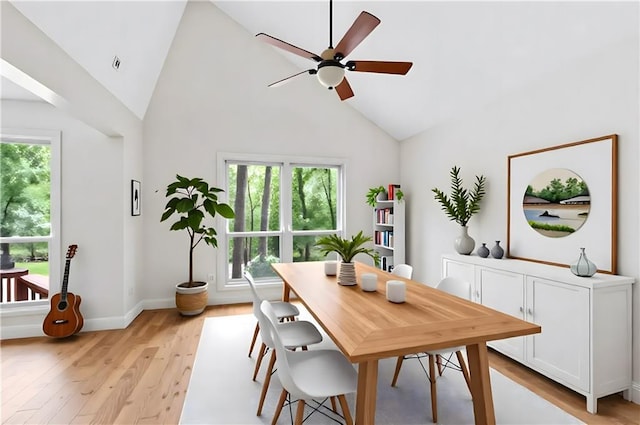 dining space with a ceiling fan, healthy amount of natural light, light wood finished floors, high vaulted ceiling, and baseboards