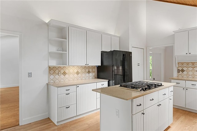 kitchen featuring freestanding refrigerator, stainless steel gas stovetop, open shelves, tasteful backsplash, and light wood finished floors