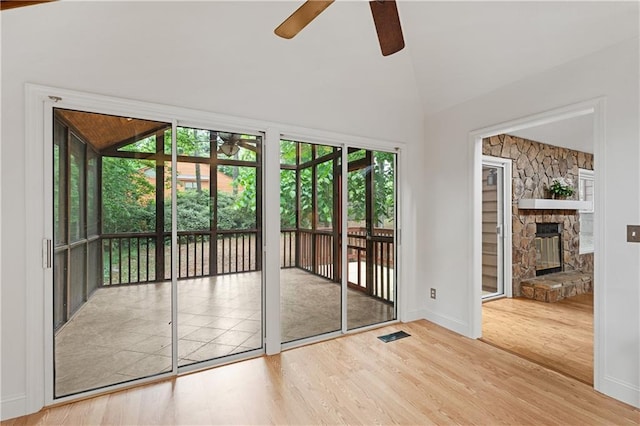 doorway to outside featuring a ceiling fan, wood finished floors, lofted ceiling, baseboards, and a stone fireplace