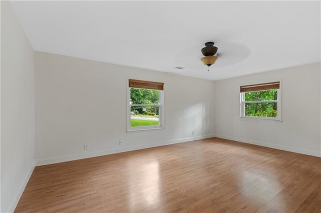 empty room featuring plenty of natural light, light wood-type flooring, baseboards, and ceiling fan