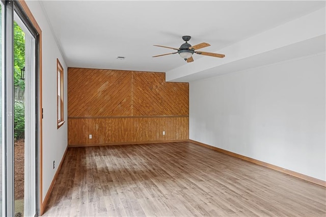 spare room featuring light wood-style flooring, wooden walls, ceiling fan, and baseboards