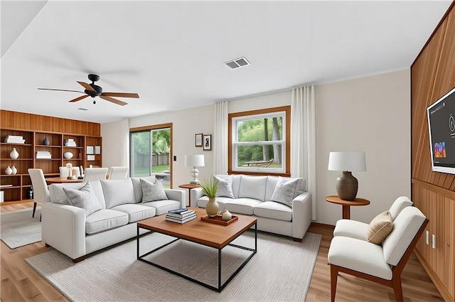 living room with light wood-style flooring, a ceiling fan, and wooden walls
