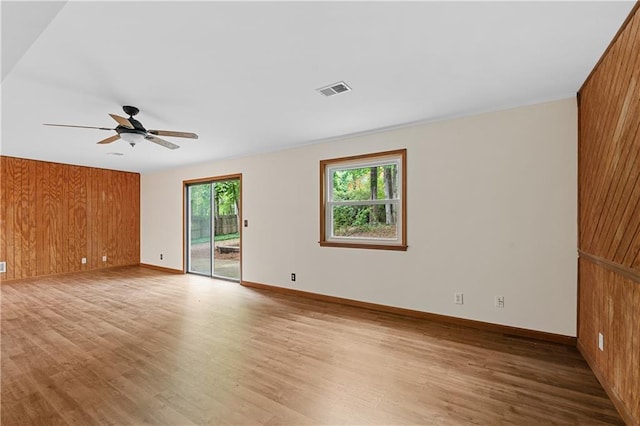 spare room with wood finished floors, ceiling fan, baseboards, and wood walls