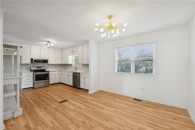 kitchen featuring appliances with stainless steel finishes, a sink, light wood finished floors, light countertops, and a chandelier