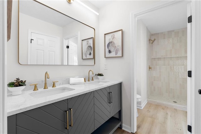 bathroom with vanity, wood-type flooring, a tile shower, and toilet