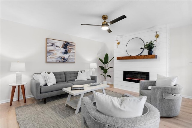 living room with ceiling fan, a large fireplace, and light hardwood / wood-style floors