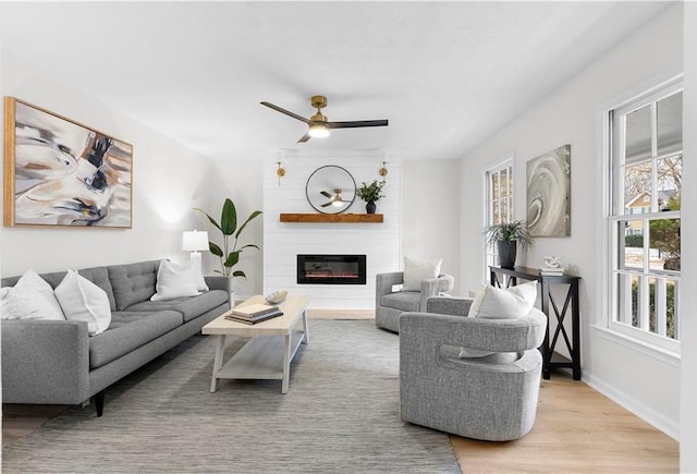 living room with ceiling fan, a large fireplace, and light hardwood / wood-style floors