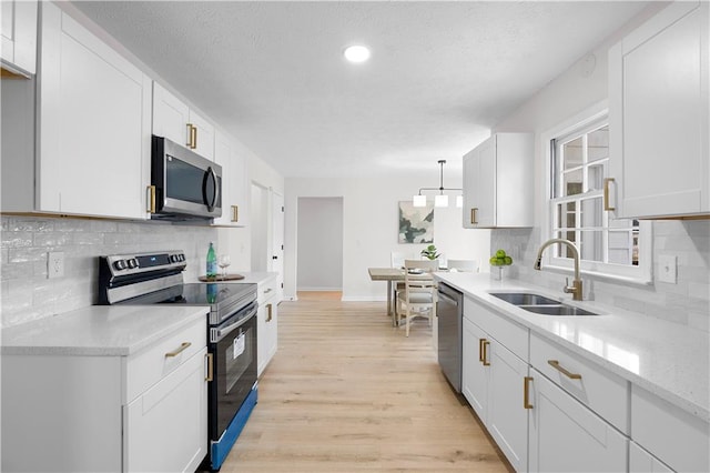 kitchen featuring white cabinetry, sink, hanging light fixtures, and appliances with stainless steel finishes