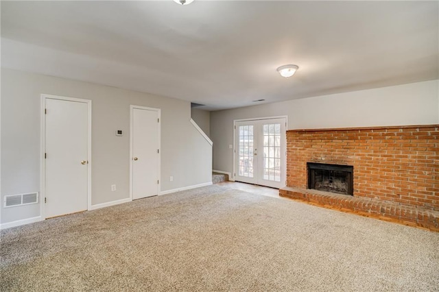 unfurnished living room featuring a brick fireplace, carpet floors, and french doors