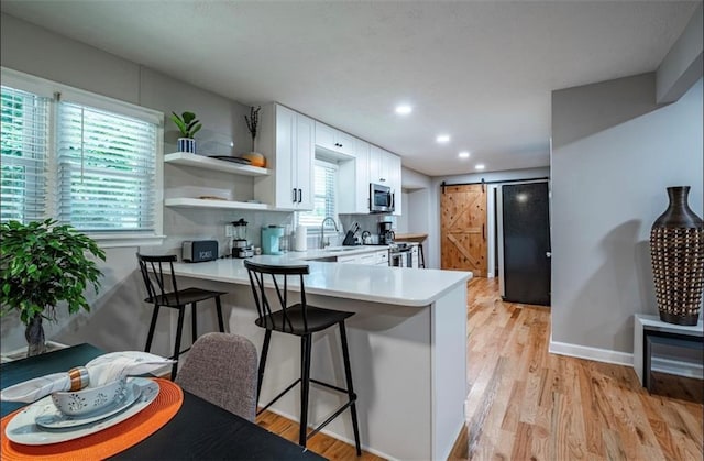 kitchen with stainless steel appliances, open shelves, light countertops, white cabinets, and a peninsula