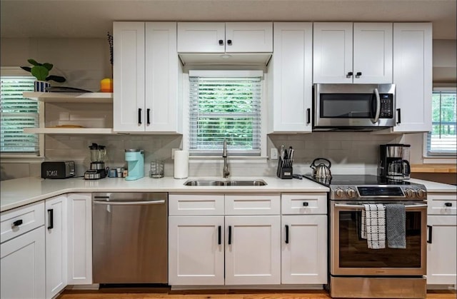 kitchen featuring appliances with stainless steel finishes, a sink, open shelves, white cabinetry, and light countertops