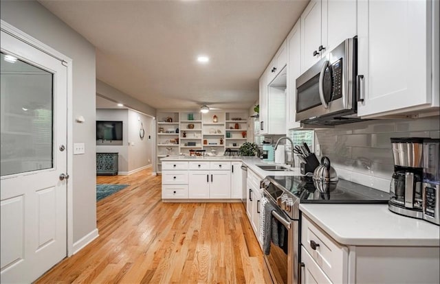 kitchen with appliances with stainless steel finishes, a sink, white cabinets, a peninsula, and light countertops