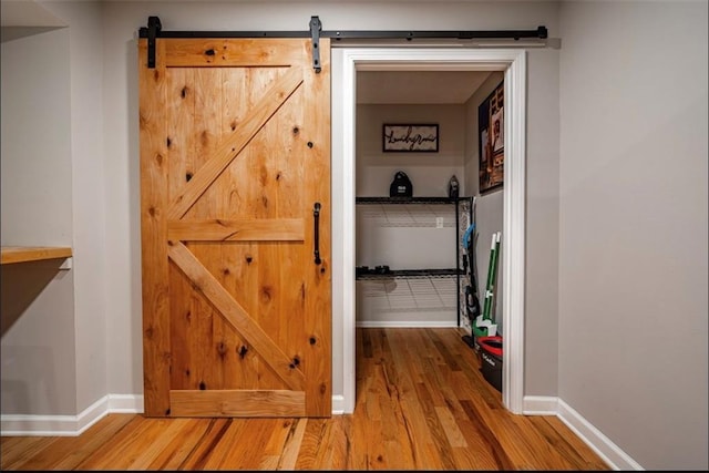 hall with wood finished floors, a barn door, and baseboards