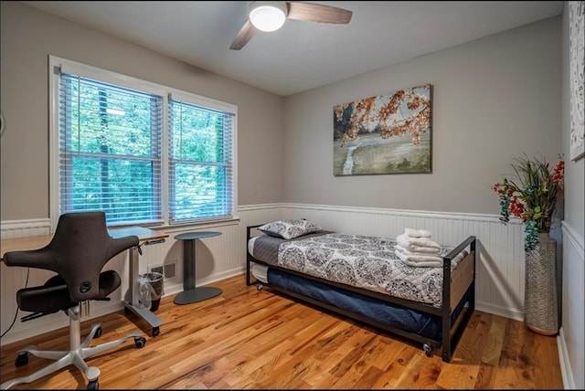 bedroom featuring a wainscoted wall, light wood-type flooring, and ceiling fan