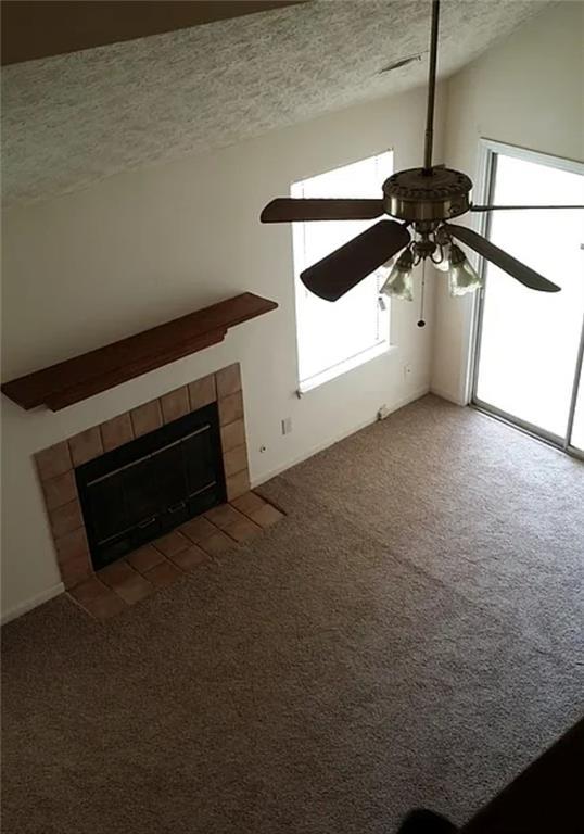 unfurnished living room featuring ceiling fan, a tiled fireplace, dark carpet, and a textured ceiling