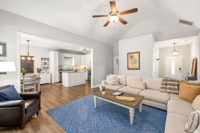 living area featuring dark wood-style flooring, lofted ceiling, visible vents, baseboards, and ceiling fan with notable chandelier