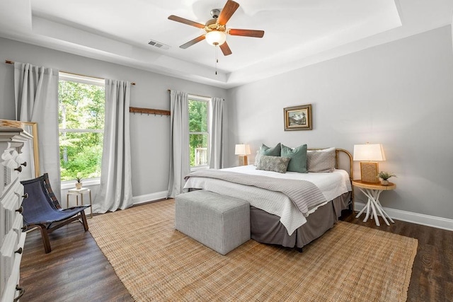 bedroom with a tray ceiling, visible vents, baseboards, and wood finished floors